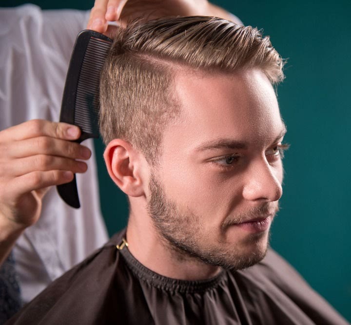 A man's hair being combed into a side part with a tapered fade