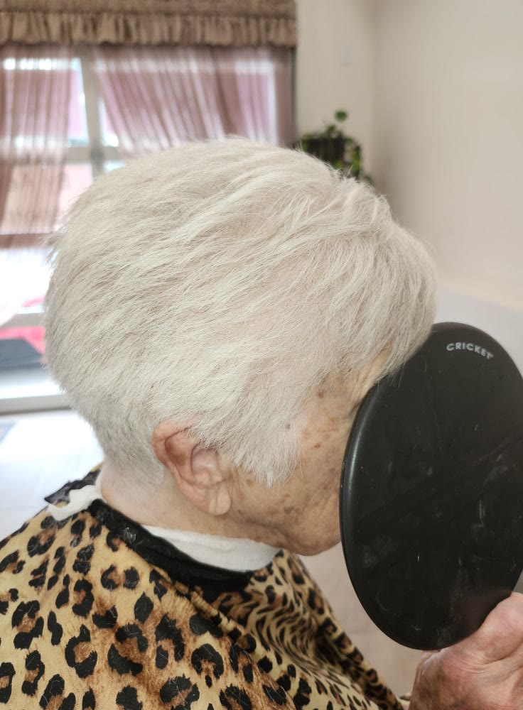 Short tapered cut on silver-white hair, as the client checks the back in a hand mirror